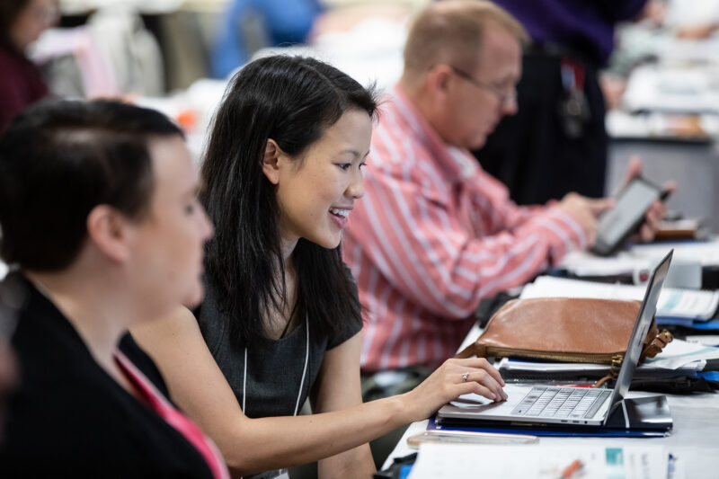 A woman listens during a meeting and uses her laptop